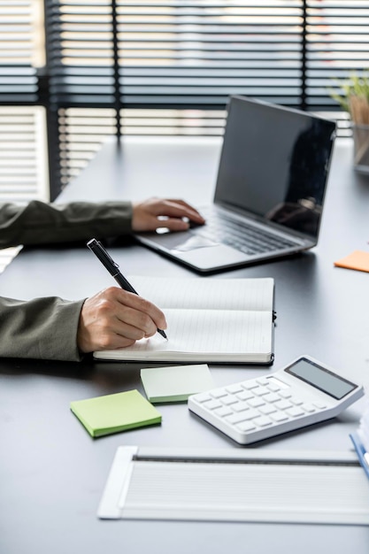 Деловая женщина пишет заметку или бизнес-план и работает на ноутбуке за своим столом в современном офисе
