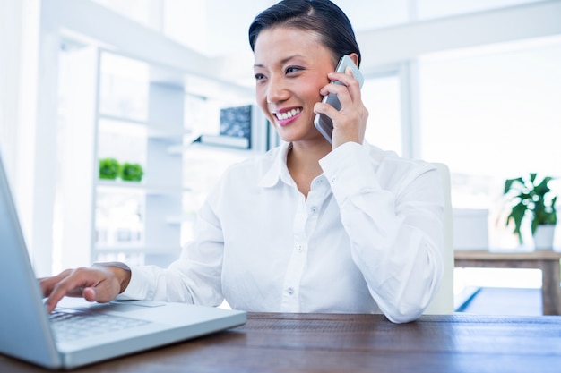 Businesswoman having phone call and using laptop computer 