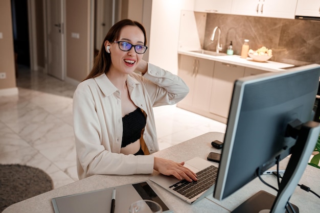 Businesswoman in headphones wearing casual clothes working at\
home office on laptop young happy female student studying in online\
university and talking with friends by video call