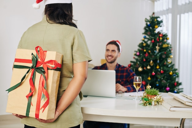 彼女の後ろに同僚のための大きな装飾されたクリスマスプレゼントを隠している実業家