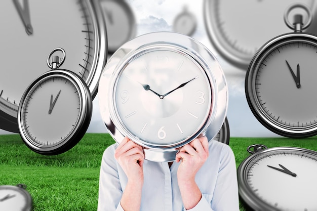 Businesswoman hiding face with clock against grey sky over field