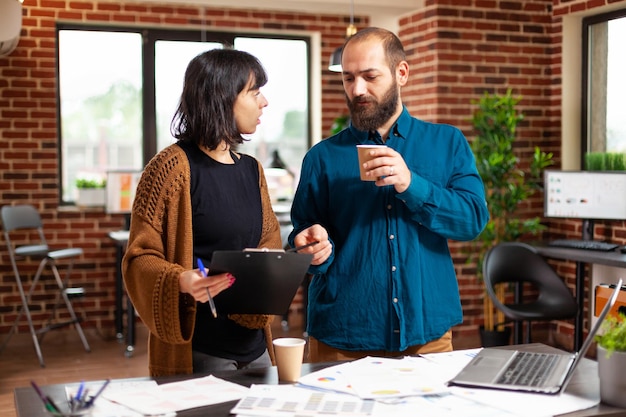 Businesswoman holding clipboard with company report explaining marketing strategy to entrepreneur man brainstorming ideas for financial project. Businesspeople analyzing documents in startup office