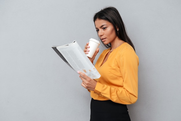 Businesswoman holding cup of coffee and reading newspaper