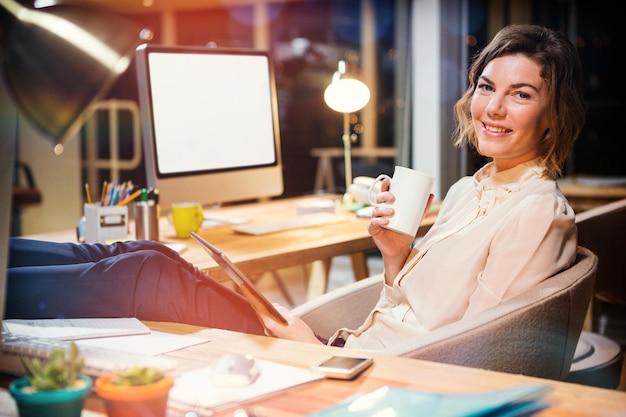 Businesswoman holding digital tablet and coffee cup at desk