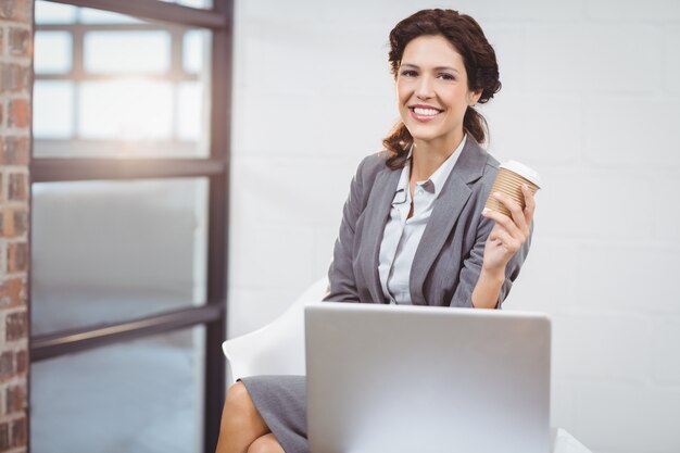 Businesswoman holding disposable cup sitting on desk