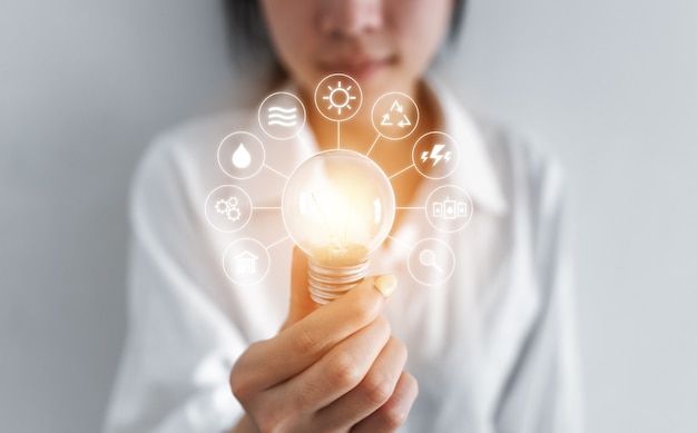 Businesswoman holding glowing light bulb, with eco-friendly energy resources icons