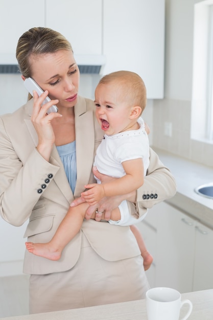 Businesswoman holding her crying baby talking on the phone