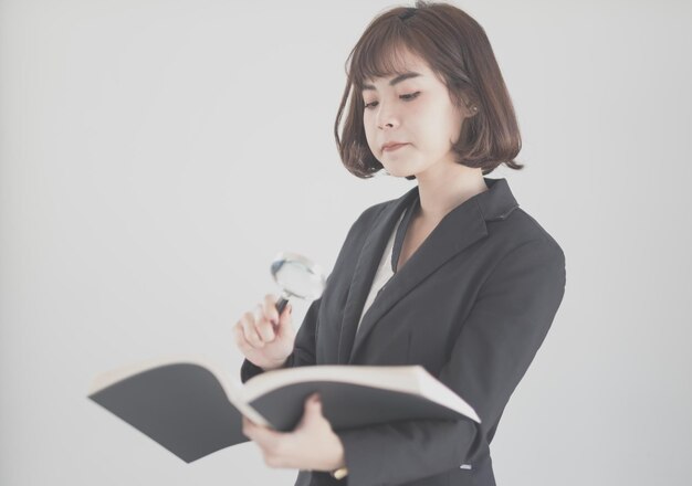 Businesswoman holding magnifying glass and book against white background