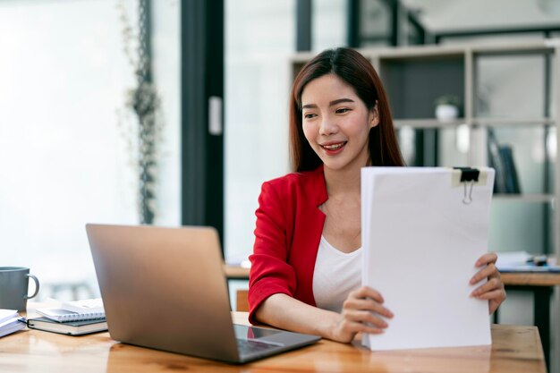 Photo businesswoman holding papers preparing report analyzing work results female executive doing paperwork at workplace using computer for data analysis