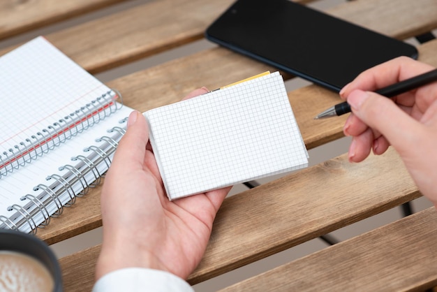 Photo businesswoman holding pen and notepad with important message on table with notebooks and phone woman presenting crutial information on paper on desk with cellphone and coffee