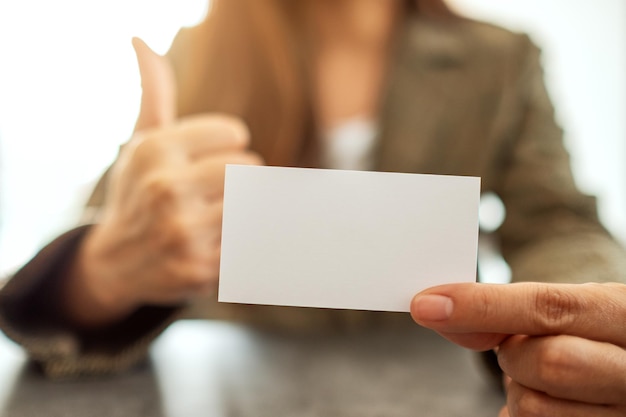 A businesswoman holding and showing a blank empty business card while making thumb up to show good sign