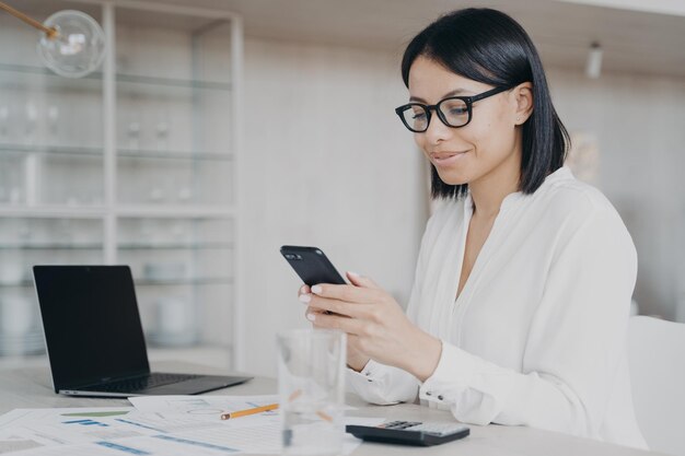 Businesswoman holding smartphone using mobile apps for ebusiness answers messages in office