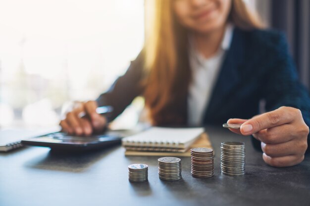 Businesswoman holding and stacking coins while calculating money on the table