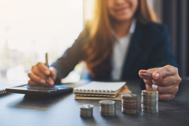 Businesswoman holding and stacking coins while calculating money on the table