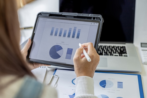 A businesswoman holding a tablet that opens the company's financial documents from the finance department, she checks the information in the documents to analyze the financial management plan.