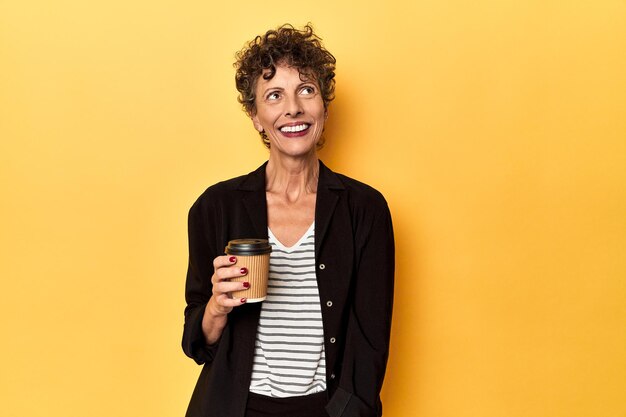 Businesswoman holding takeaway coffee on yellow dreaming of achieving goals and purposes