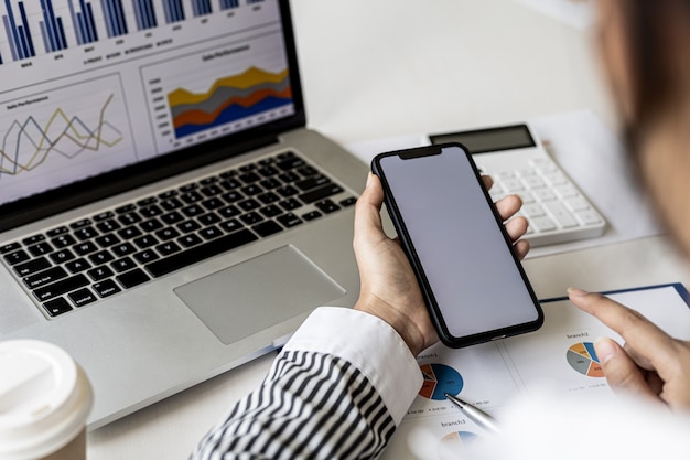 A businesswoman is holding a smartphone and using it, she is using a smartphone to send text messages to a company partner about financial statements. Concept of using technology in communication.