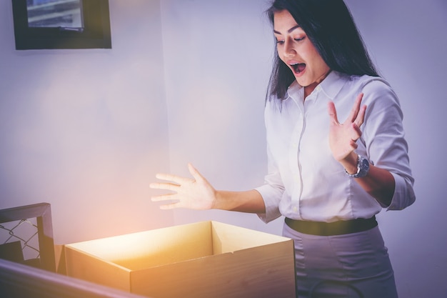 Businesswoman is opening cardboard box with surprise emotion for something inside.