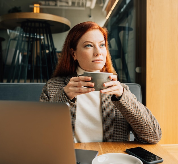 Businesswoman in a jacket holding a cup sitting at cafe in the morning