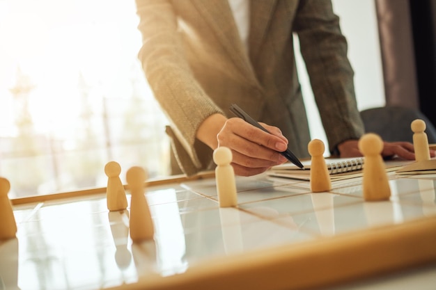 Businesswoman leader writing and choosing wooden people from a group of employees on a planning board