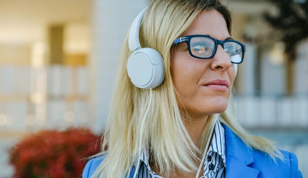 Бизнесменка слушает музыку в наушниках напротив офисного здания