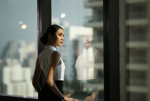 businesswoman looking away while standing by window at office
