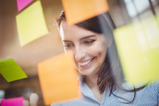 Businesswoman looking at sticky notes stuck to glass