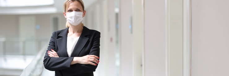 Photo businesswoman in medical protective mask stands with folded arms in hotel corridor
