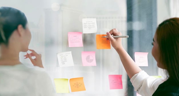 Businesswoman meeting at office and use sticky notes on glass wall in office planning work together brainstorm strategy