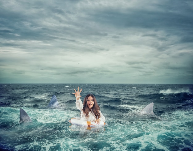 Businesswoman in the ocean with lifebelt surrounded by sharks asks help