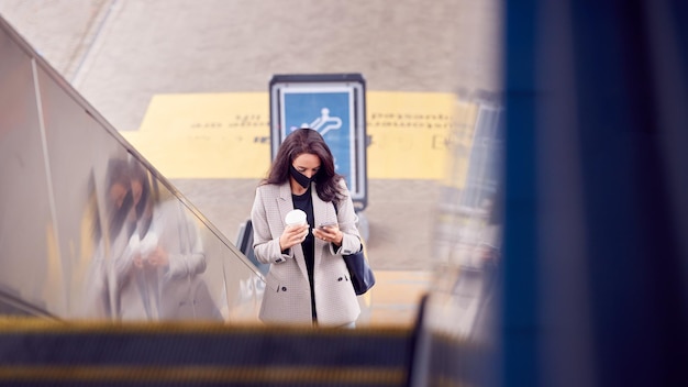 사진 전염병에 ppe 얼굴 마스크를 착용하는 휴대 전화와 기차역에서 에스컬레이터에 사업가