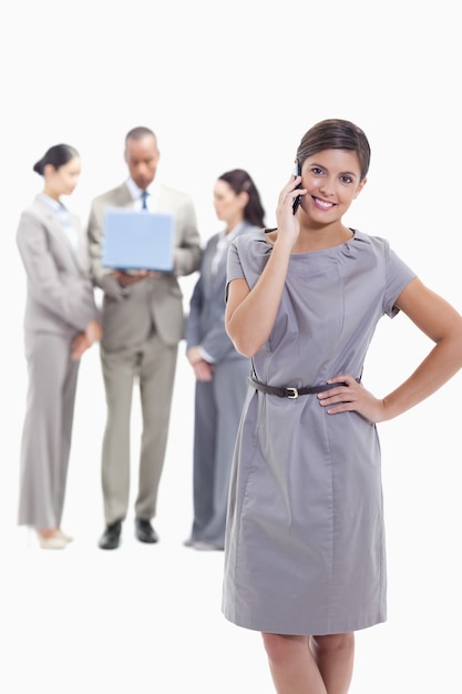Businesswoman on the phone with a hand on her hip and the head tilted with co-workers in the backgro