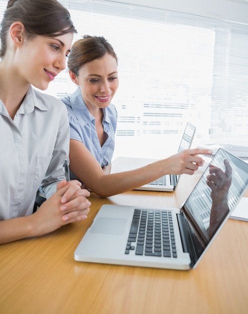 Businesswoman pointing to something on laptop for colleague