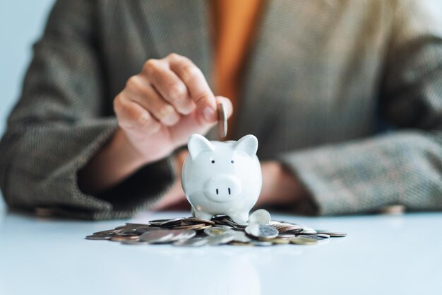 A businesswoman putting coin into piggy bank with pile of coins on the table for saving money and financial concept