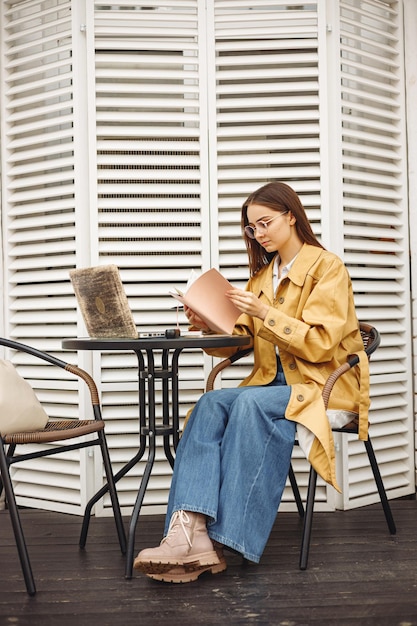 Businesswoman reading notes in notepad while sitting at table with laptop during work in urban cafe