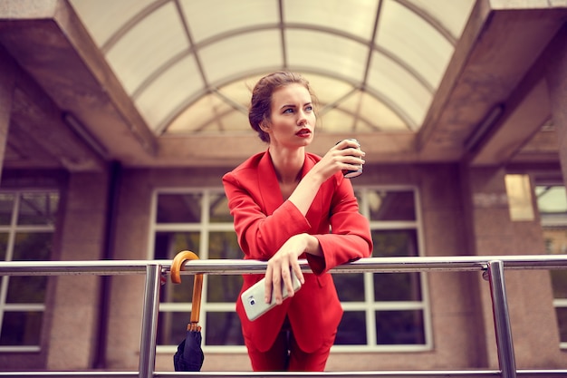 Businesswoman in red costume using mobile phone near modern building.