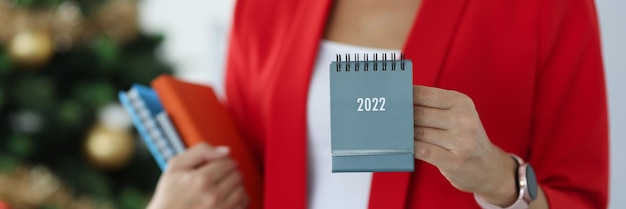 Businesswoman in red jacket holds calendar for against background of new year tree business