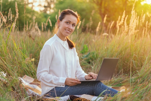 A businesswoman remotely manages a department sitting in a park with a laptop on her lap