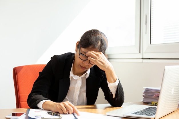 Businesswoman resting hands on head with eyes close at work desk in office.