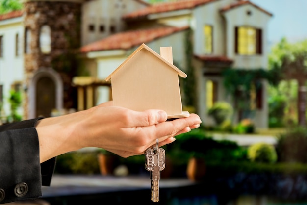 Photo businesswoman's hand holding wooden house model and keys against blur house