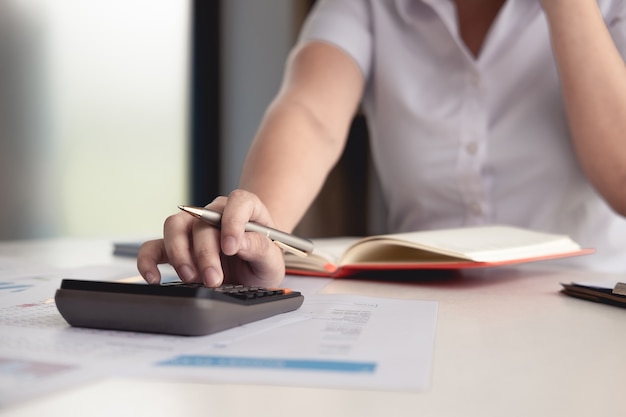 Le mani della donna di affari con il calcolatore all'ufficio e ai dati finanziari che analizzano conteggio