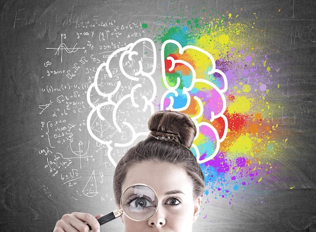Businesswoman s head with a magnifying glass near her eye. A blackboard with a colorful brain sketch on it.
