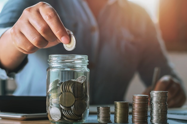 businesswoman saving money by hand puting coins in jug glass