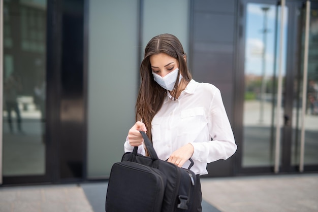 Businesswoman searching for something in her laptop bag during covid and coronavirus pandemic