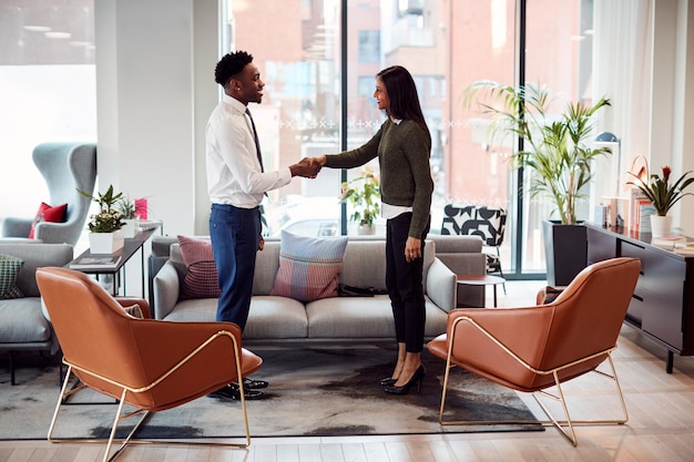 Businesswoman Shaking Hands With Male Interview Candidate In Seating Area Of Modern Office