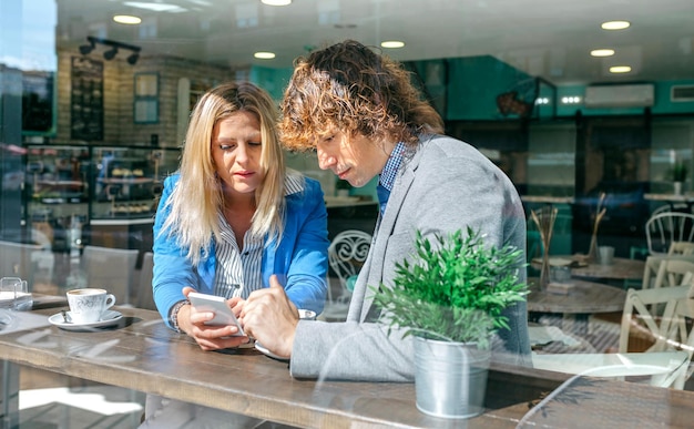 Businesswoman showing something on the phone to coworker in a coffee shop