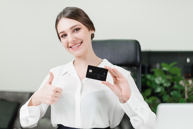 Коммерсантка показывает кредитную карточку и большие пальцы руки вверх в офисе