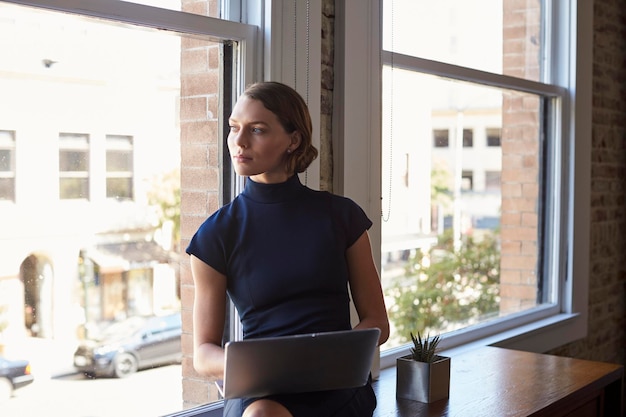 Businesswoman Sitting By Window Working On Laptop