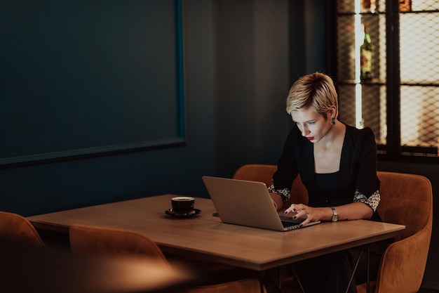 Бизнесменка, сидящая в кафе, сосредоточенная на работе на ноутбуке и участвующая в онлайн-встречах.