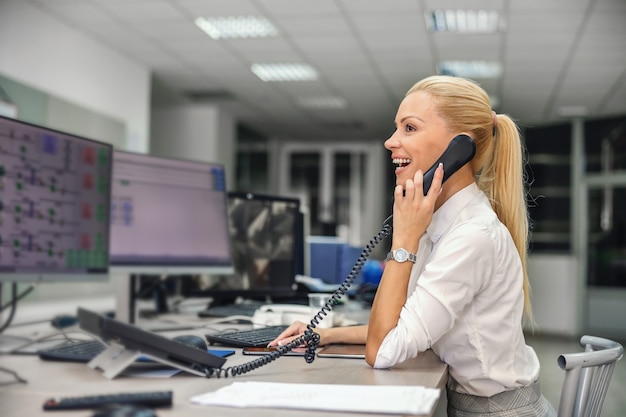 Businesswoman sitting in control room in heating plant and having phone conversation with her boss.